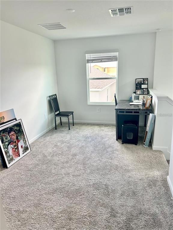 A carpeted home office features a desk, a chair, and a framed poster on the floor — 572 REGGIE ROAD, WINTER HAVEN, FL