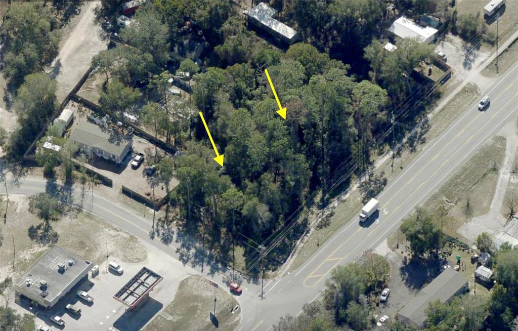 An aerial view shows a wooded, undeveloped lot bordered by a road and nearby buildings — LOT 13 STATE ROAD 44, EUSTIS, FL