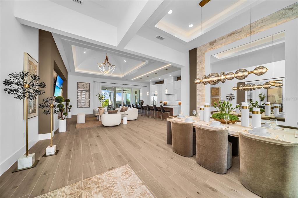 An open-concept living and dining area features light wood floors, coffered ceilings, and modern decor — 6264 CHAMPIONS ROW STREET, BRADENTON, FL