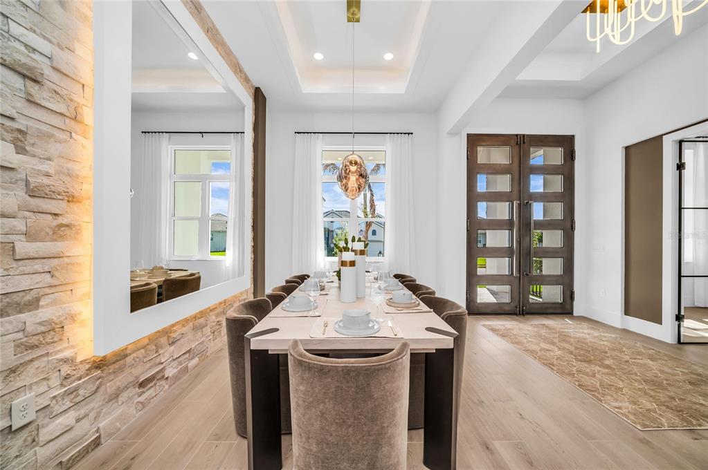 A dining room features a long table, upholstered chairs, a stone accent wall, and double doors — 6264 CHAMPIONS ROW STREET, BRADENTON, FL