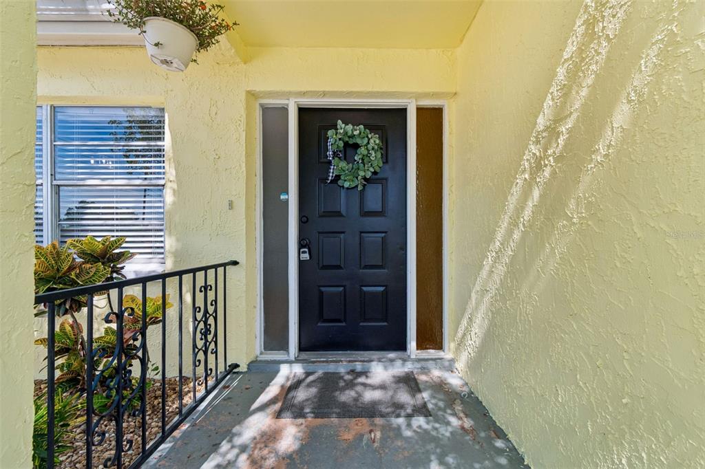 A black front door with a wreath is centered on a yellow porch with railings — 9631 MARLINTON LANE, PORT RICHEY, FL