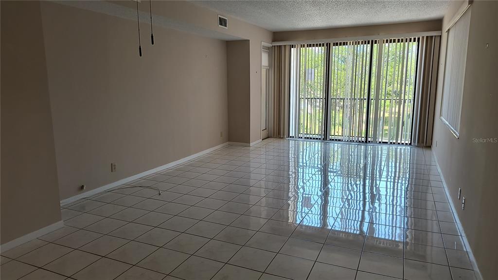 An empty living room features light-colored tile flooring, beige walls, and large floor-to-ceiling windows — 8 BELLEVIEW BOULEVARD UNIT 202, BELLEAIR, FL
