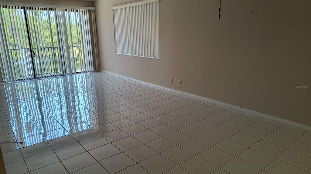 An empty room features light-colored tile flooring, vertical blinds, and a sliding glass door — 8 BELLEVIEW BOULEVARD UNIT 202, BELLEAIR, FL