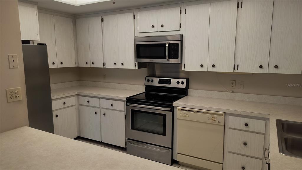 A kitchen features white cabinets, stainless steel appliances, a beige dishwasher, and light-colored countertops — 8 BELLEVIEW BOULEVARD UNIT 202, BELLEAIR, FL