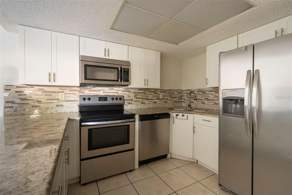 A kitchen with white cabinets, stainless steel appliances, granite countertops, and a tiled backsplash — 1649 SUNNY BROOK LANE NE UNIT B105, PALM BAY, FL