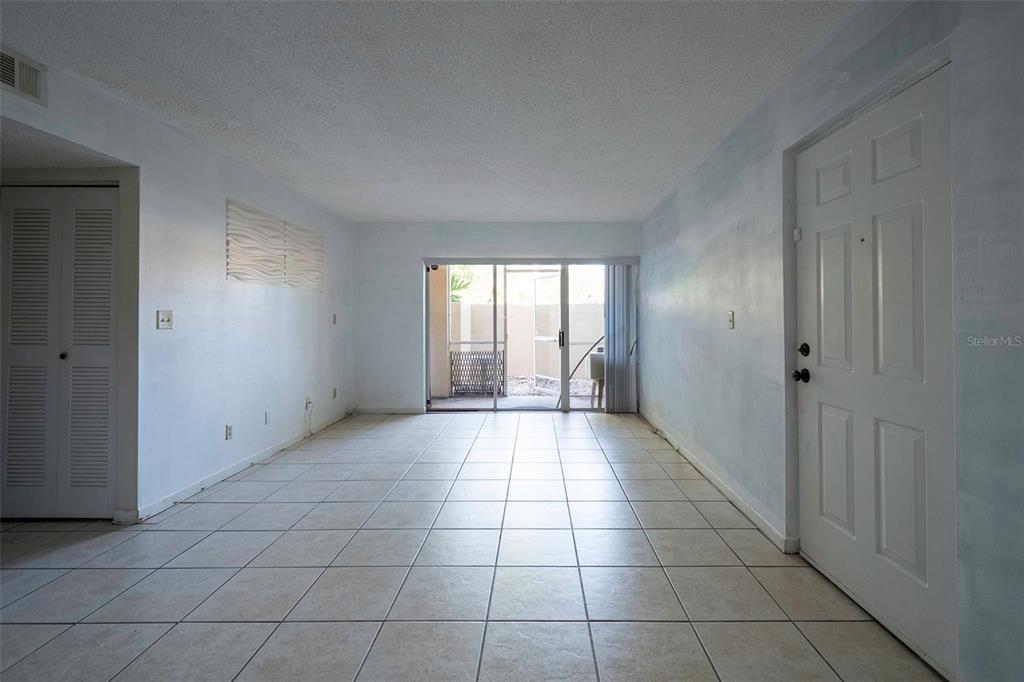An empty living room features white walls, tile flooring, and a sliding glass door to a patio — 1649 SUNNY BROOK LANE NE UNIT B105, PALM BAY, FL