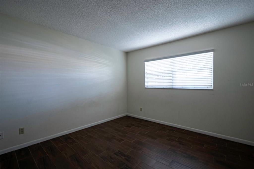 An empty bedroom features white walls, a single window with blinds, and dark wood-look flooring — 1649 SUNNY BROOK LANE NE UNIT B105, PALM BAY, FL