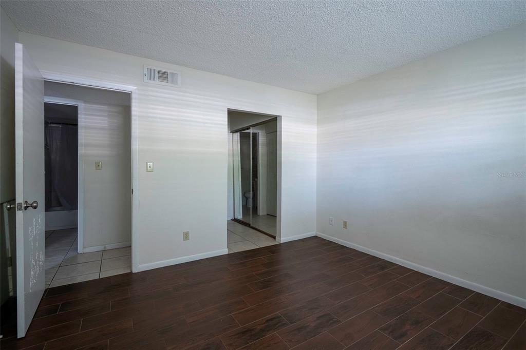 An empty bedroom features dark wood-look tile flooring, white walls, and two doorways — 1649 SUNNY BROOK LANE NE UNIT B105, PALM BAY, FL