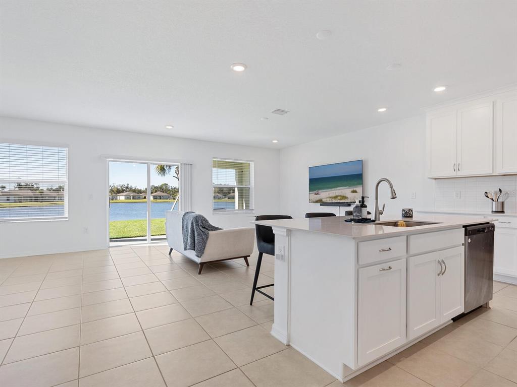 A bright kitchen and living area with white cabinets, a center island, and lake views — 9975 LAST LIGHT GLEN, PARRISH, FL