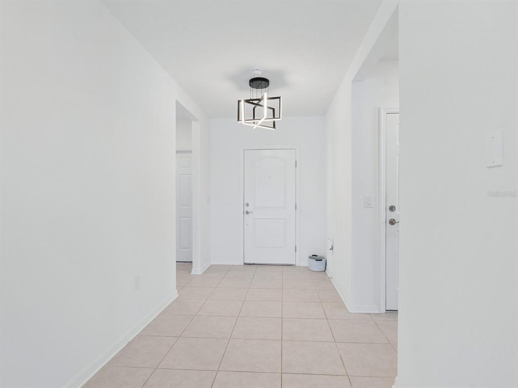 An entryway features white walls, tile flooring, a modern light fixture, and two white doors — 9975 LAST LIGHT GLEN, PARRISH, FL