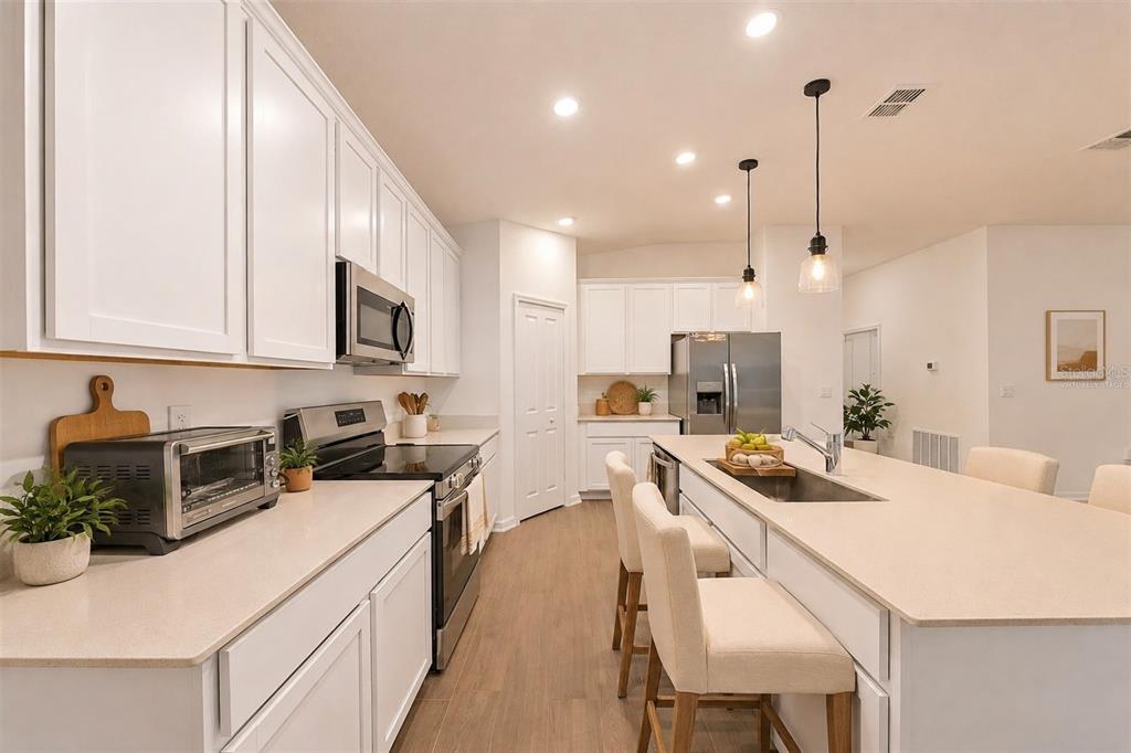 A kitchen with white cabinets, stainless steel appliances, and a large island with quartz countertops — 3977 WILLOWBROOK DRIVE, EDGEWATER, FL