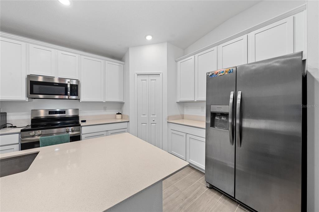 A modern kitchen features white cabinetry, stainless steel appliances, a center island, and wood-look flooring — 3977 WILLOWBROOK DRIVE, EDGEWATER, FL