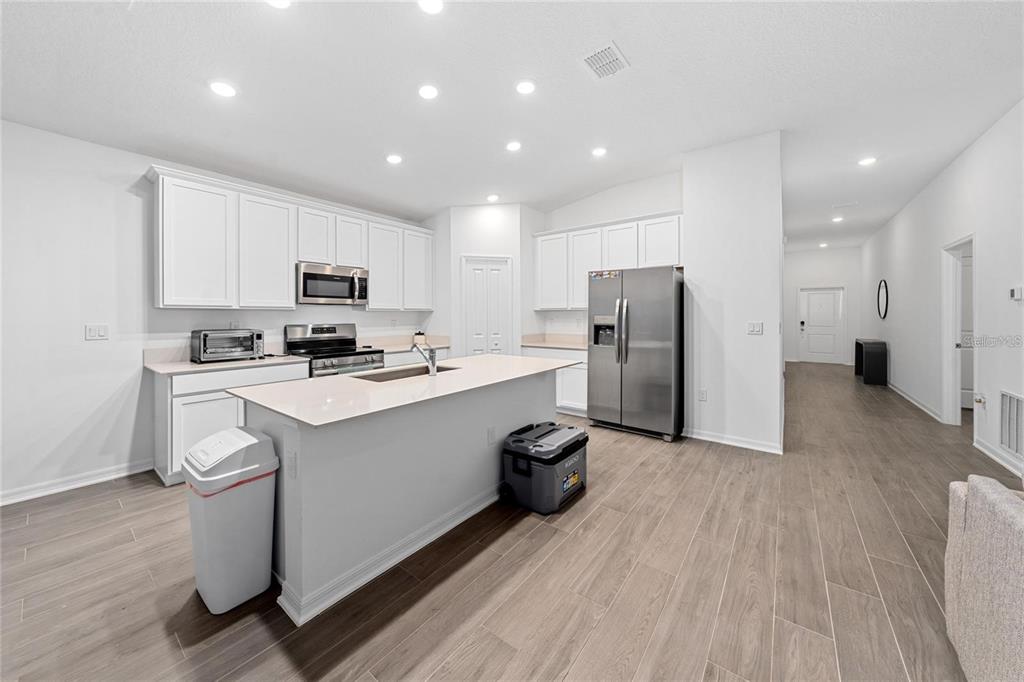 A modern kitchen features white cabinetry, a central island with bar seating, and stainless steel appliances — 3977 WILLOWBROOK DRIVE, EDGEWATER, FL
