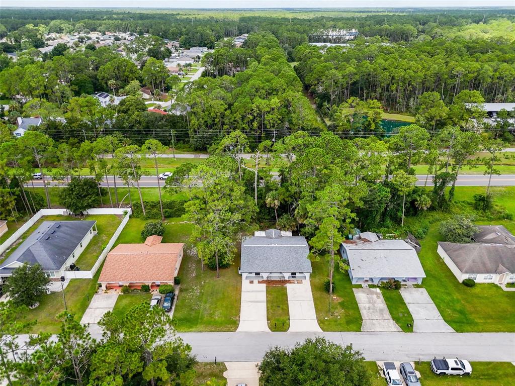 An aerial view shows three suburban houses with driveways facing a street near a wooded area — 33 WELLWOOD LANE, PALM COAST, FL