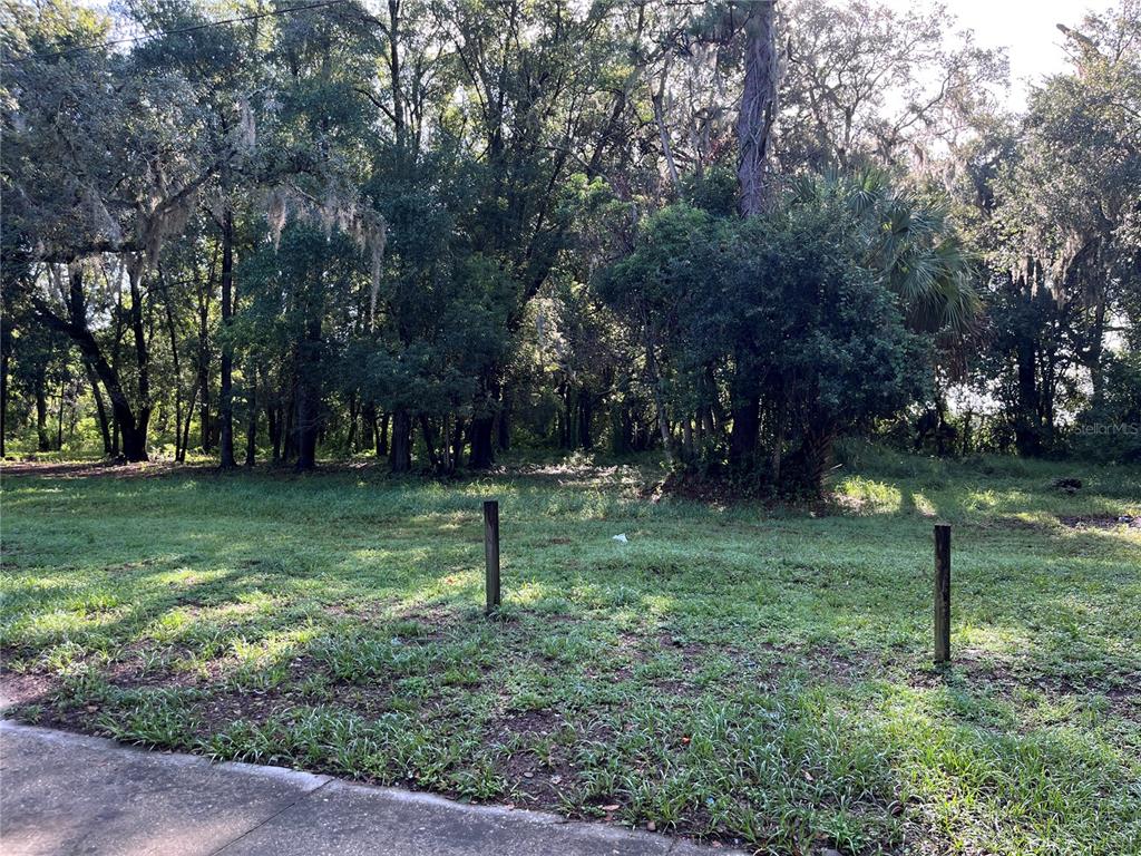 A grassy, partially wooded vacant lot features two wooden posts in the foreground — 325 MARKER STREET, ALTAMONTE SPRINGS, FL