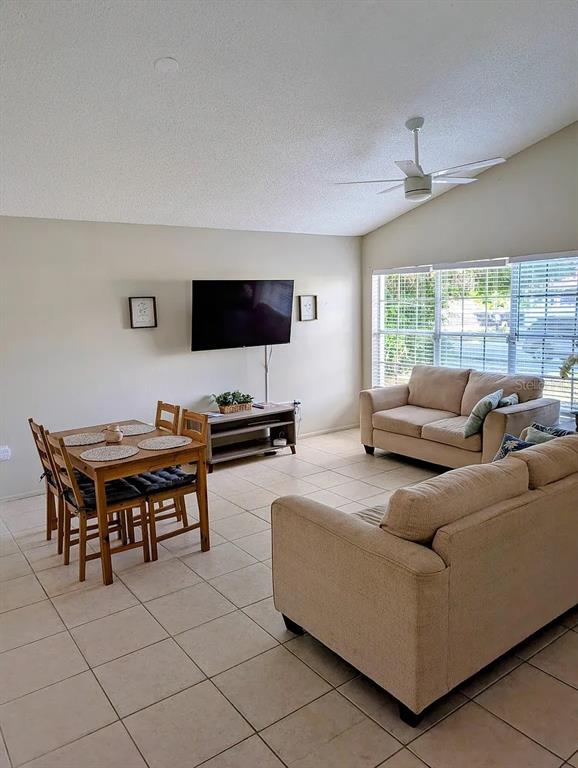 A living room and dining area with tile floors, beige sofas, and a wall-mounted television — 1083 SNEAD AVENUE, SARASOTA, FL