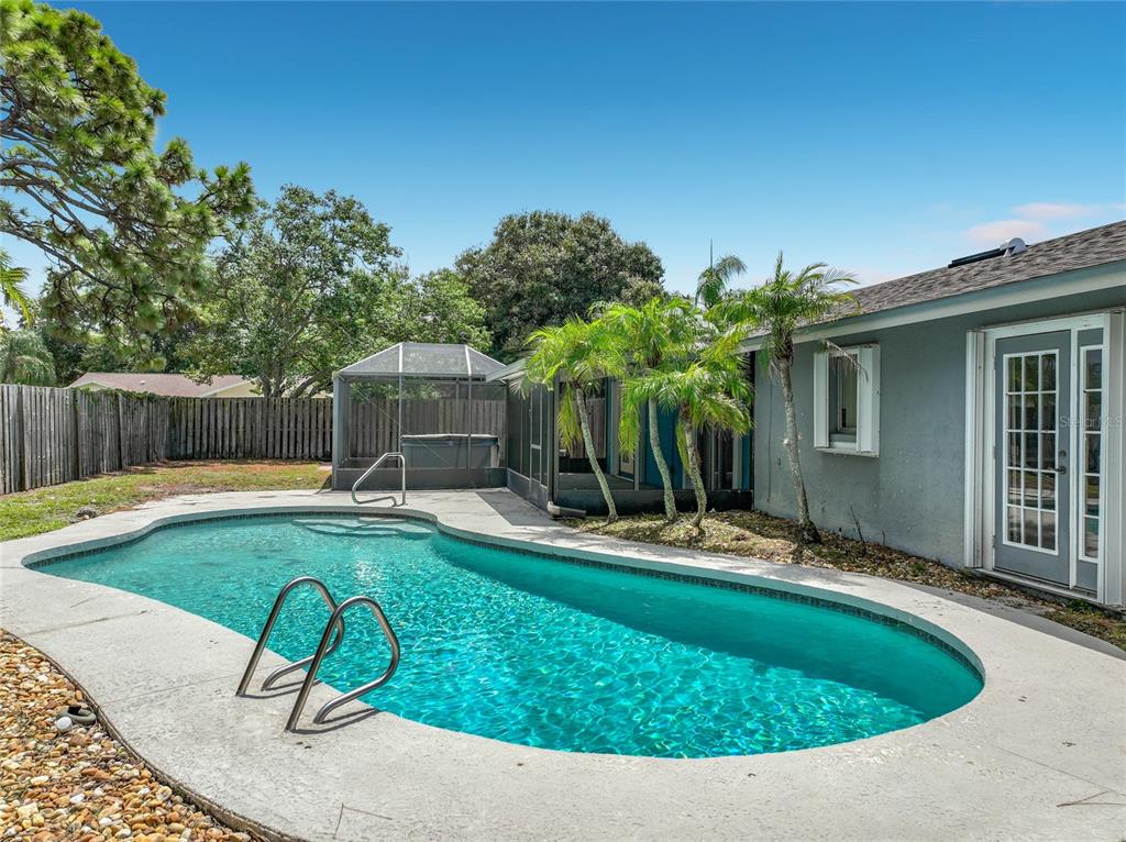 A backyard features a kidney-shaped swimming pool, a screened-in hot tub, and a gray house — 2983 ONTARIO CIRCLE W, MELBOURNE, FL