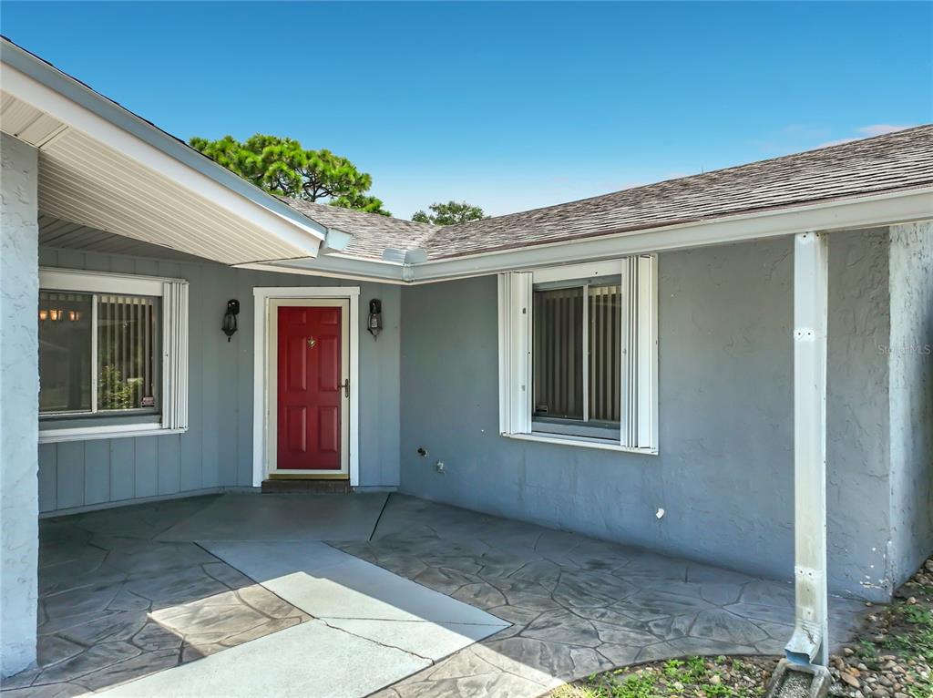 A gray house exterior features a red front door, a covered patio, and two windows — 2983 ONTARIO CIRCLE W, MELBOURNE, FL