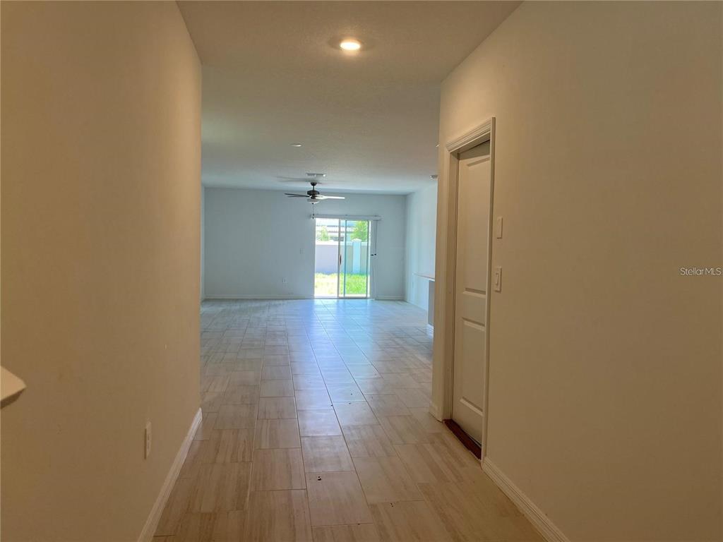 A hallway with light-colored tile flooring leads to an open living area with sliding doors — 11186 RADIANT SHORE LOOP, SAN ANTONIO, FL