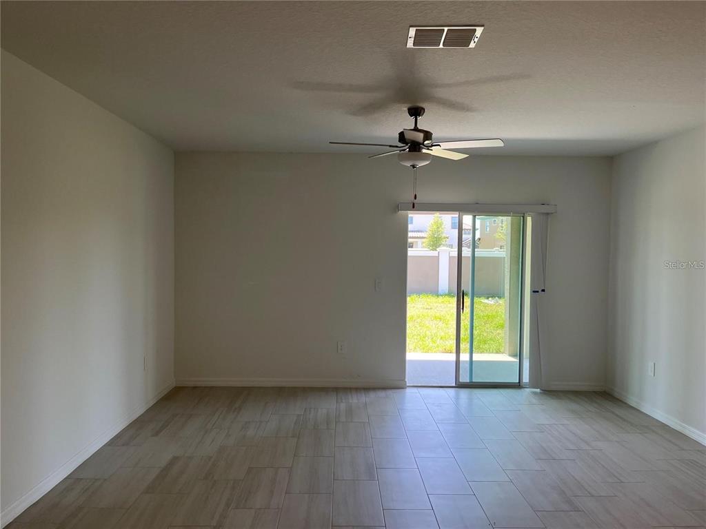 An empty room features light-colored tile flooring, a ceiling fan, and sliding glass patio doors — 11186 RADIANT SHORE LOOP, SAN ANTONIO, FL