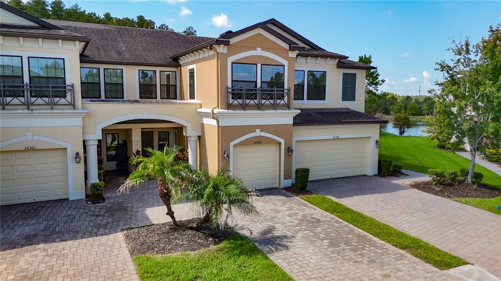 An exterior view of a two-story townhouse complex with beige stucco walls and paved driveways — 30305 SOUTHWELL LANE, WESLEY CHAPEL, FL