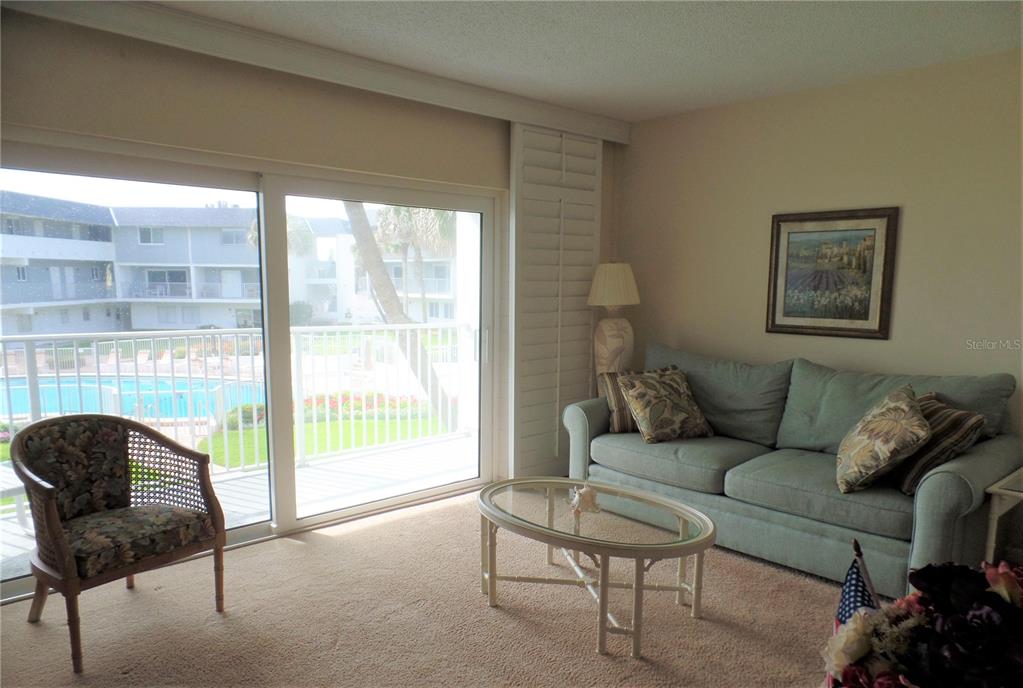 A living room features a blue sofa, a glass coffee table, and a sliding glass door — 815 OCEAN SHORE BOULEVARD UNIT 9B, ORMOND BEACH, FL