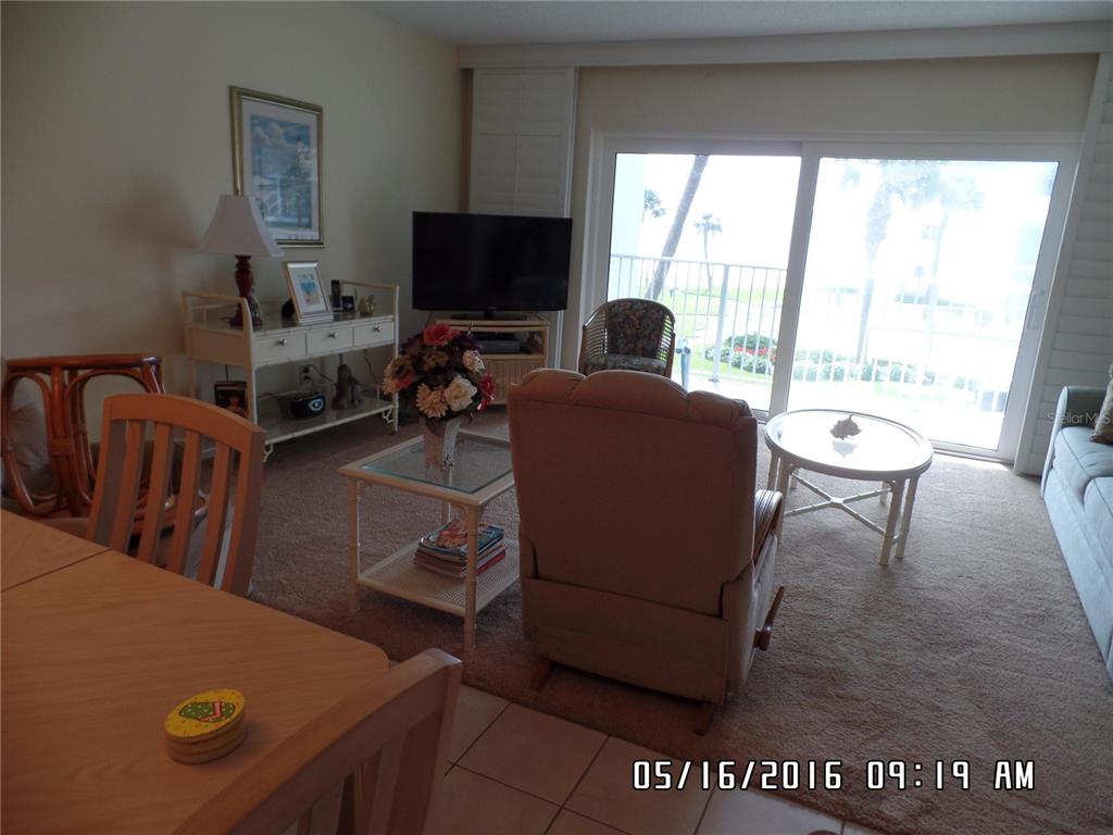 A living room features a beige recliner, glass-topped tables, a television, and sliding glass doors — 815 OCEAN SHORE BOULEVARD UNIT 9B, ORMOND BEACH, FL