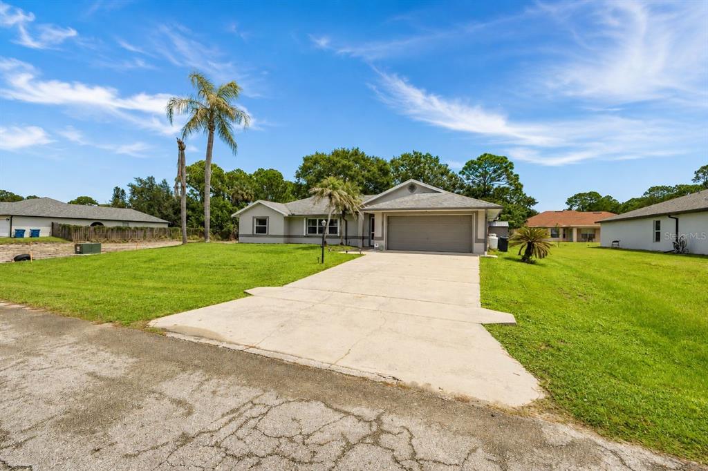 A single-story house with a concrete driveway, a two-car garage, and palm trees — 1299 AMADOR AVENUE NW, PALM BAY, FL