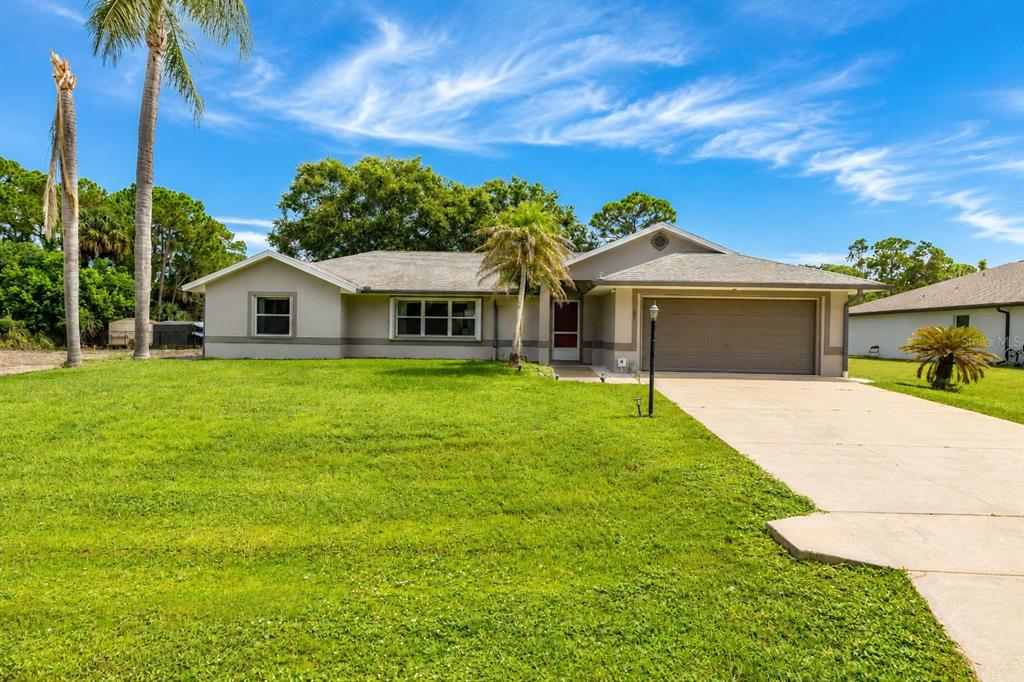A single-story house with a beige exterior, a two-car garage, and a large front lawn — 1299 AMADOR AVENUE NW, PALM BAY, FL