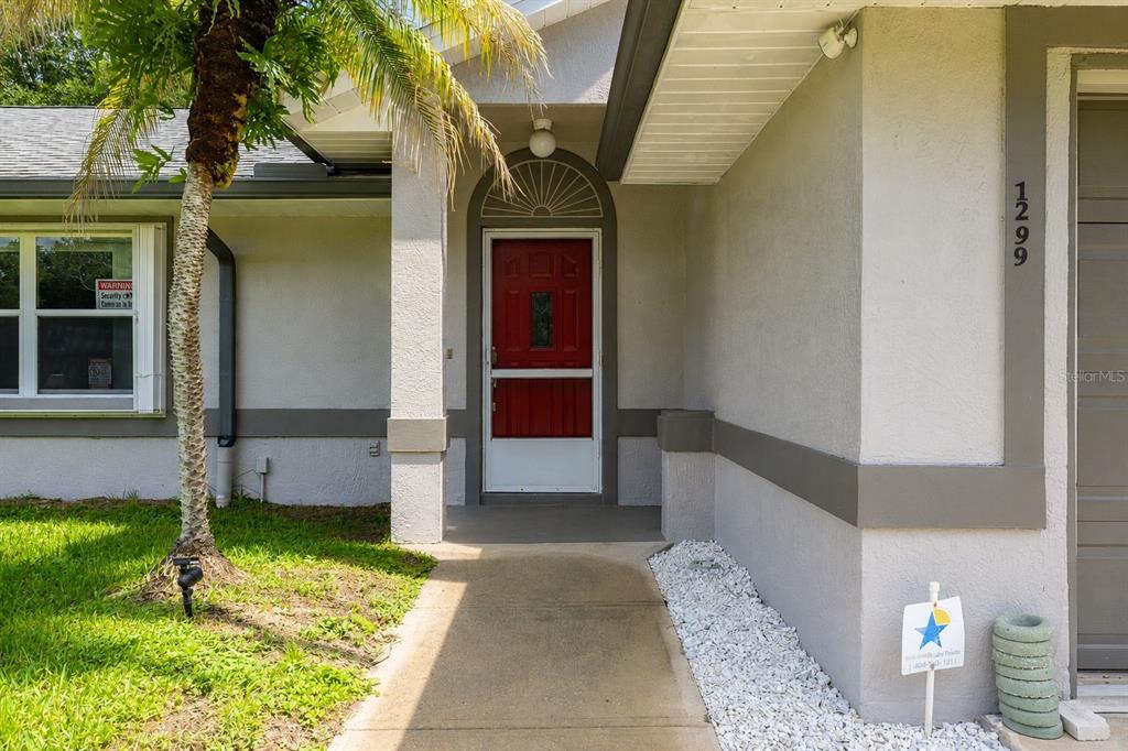A concrete walkway leads to a red front door under a covered entryway — 1299 AMADOR AVENUE NW, PALM BAY, FL