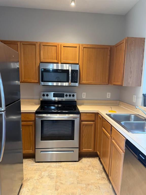 A kitchen features light wood cabinets, white appliances, and a double sink under a window — 6037 SCOTCHWOOD GLEN UNIT 8, ORLANDO, FL