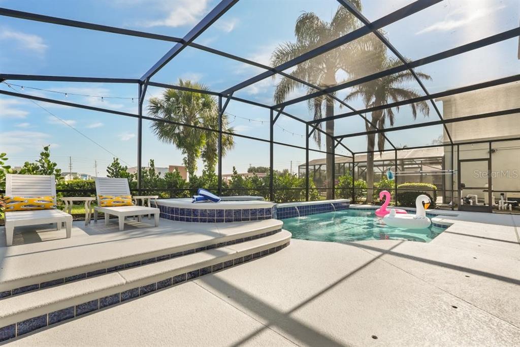 A screened-in patio features a swimming pool, a raised spa, and two lounge chairs — 8009 ACADIA ESTATES COURT, KISSIMMEE, FL