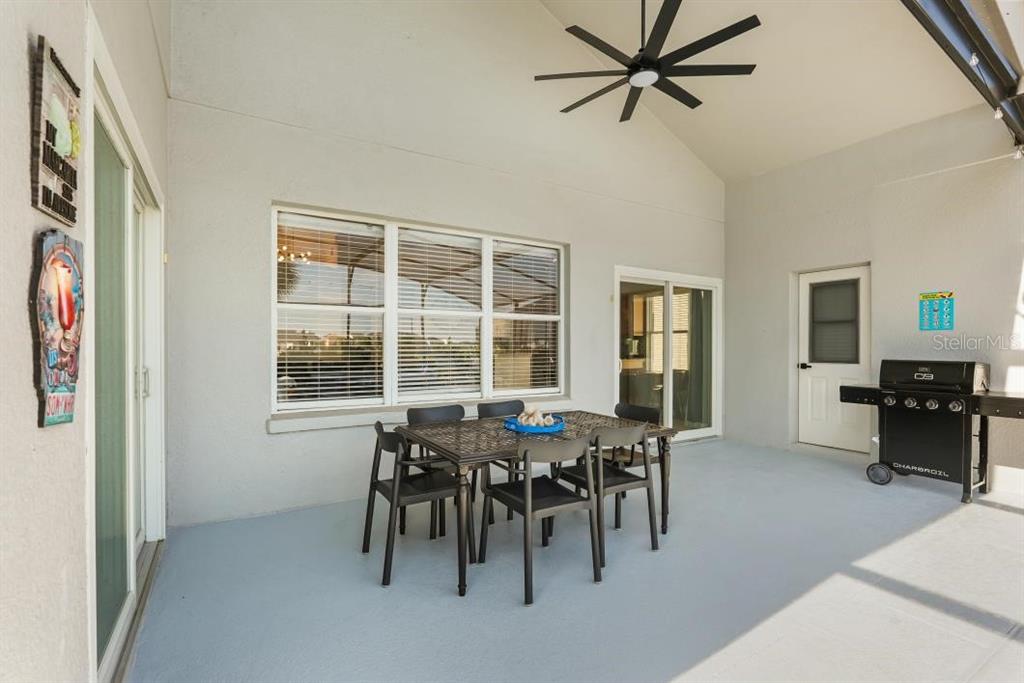 A covered patio features a dining set, a ceiling fan, and a grill — 8009 ACADIA ESTATES COURT, KISSIMMEE, FL