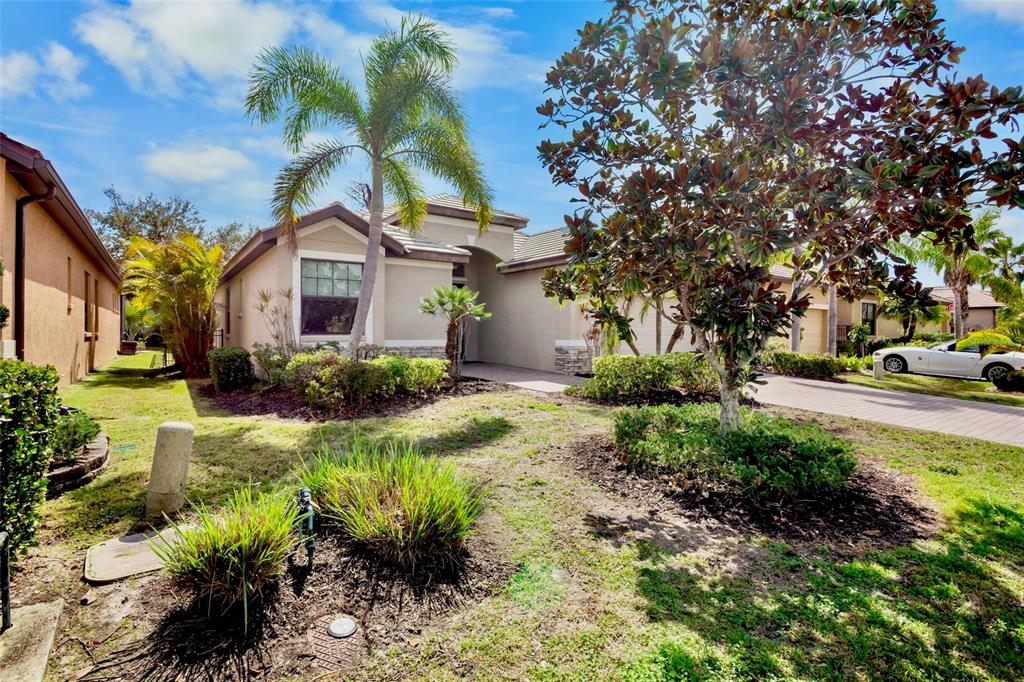 The exterior of a beige house features a paved walkway, a garage, and palm trees — 7608 RIO BELLA, BRADENTON, FL