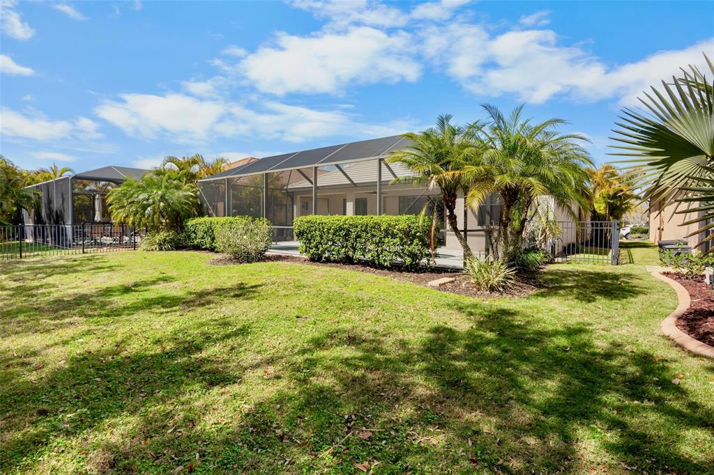 A backyard view of a house with a screened-in patio and palm trees — 7608 RIO BELLA, BRADENTON, FL