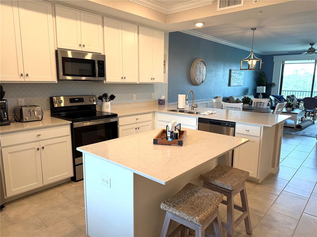 A kitchen features white cabinetry, a central island with bar stools, and light-colored countertops — 17902 GAWTHROP DRIVE UNIT 304, LAKEWOOD RANCH, FL