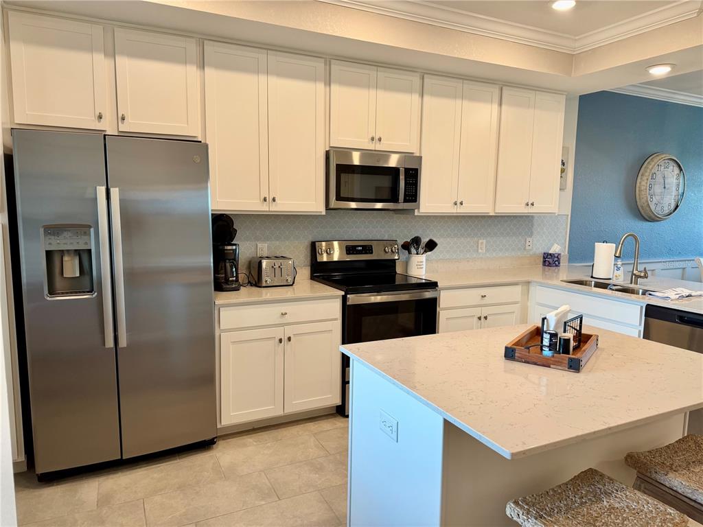 A kitchen with white cabinets, stainless steel appliances, a quartz island, and a tile backsplash — 17902 GAWTHROP DRIVE UNIT 304, LAKEWOOD RANCH, FL