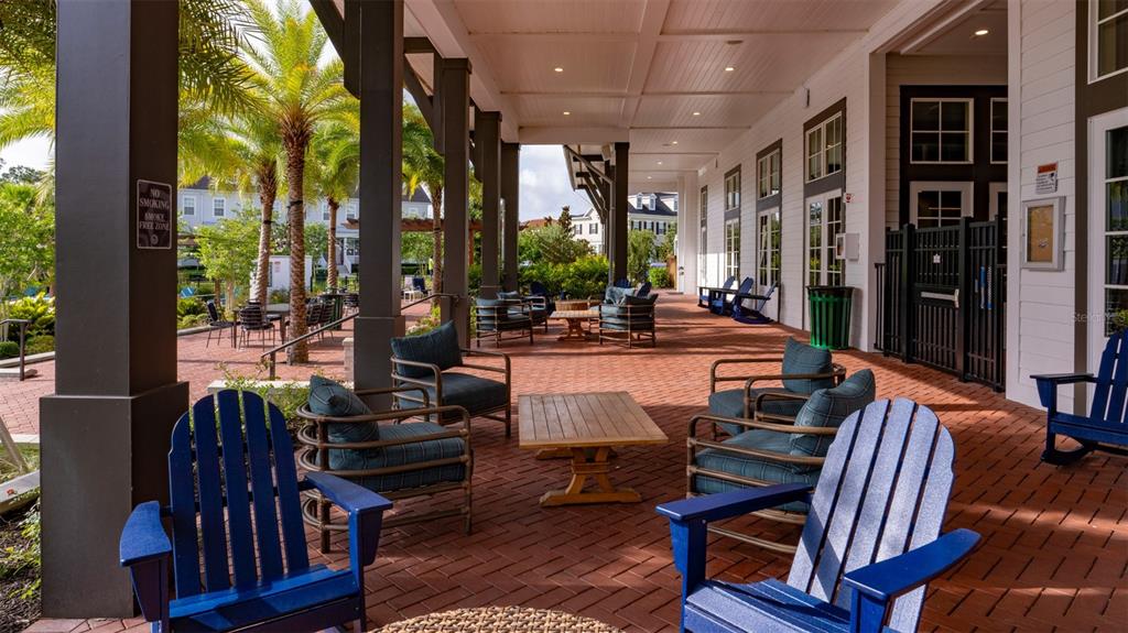 A covered brick patio features blue Adirondack chairs, lounge seating, and palm trees outdoors — 1801 ISLAND VILLAGE WAY UNIT 307, CELEBRATION, FL