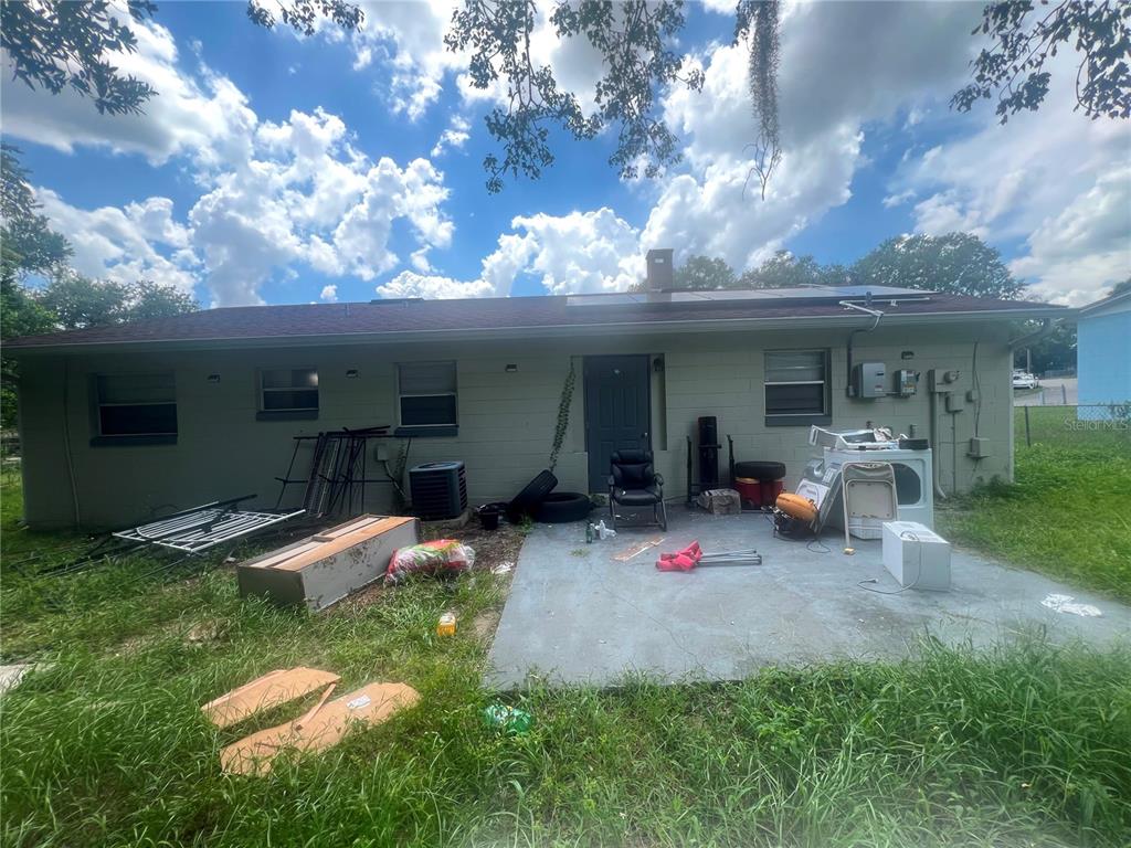 The exterior rear view of a single-story house features a concrete patio and overgrown grass — 833 LONGVIEW AVENUE, DELAND, FL