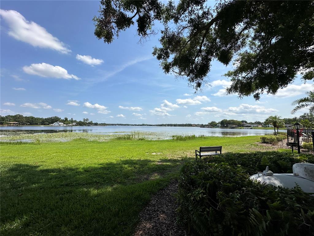 A grassy lawn leads to a lake with a bench and trees under a blue sky — 13709 JUNIPER BLOSSOM DRIVE UNIT 0, TAMPA, FL