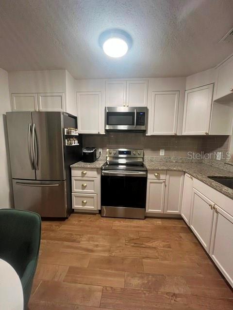 A kitchen features white cabinets, stainless steel appliances, granite countertops, and wood-look tile flooring — 3444 GELDING COURT, PORT ORANGE, FL