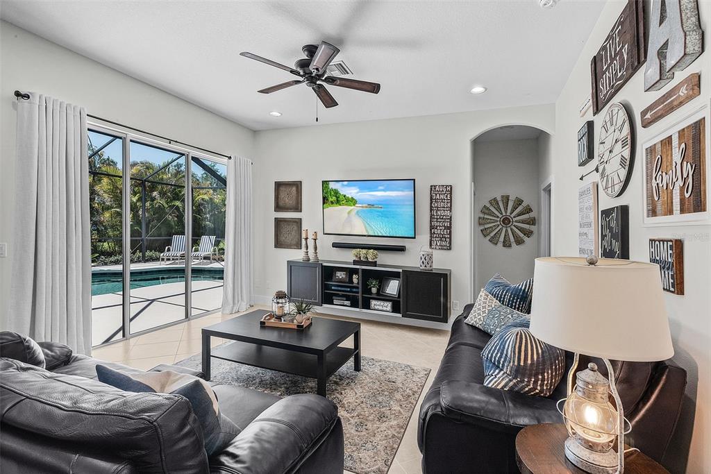 A living room with a dark leather sofa, television, and sliding doors opening to a pool — 3015 160TH TERRACE E, PARRISH, FL