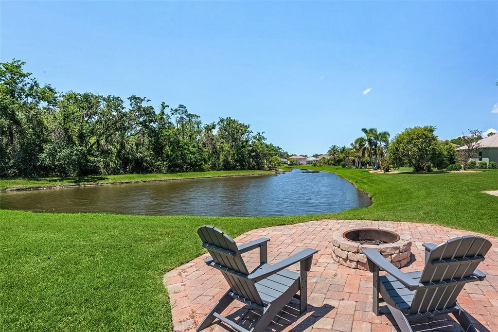 Two Adirondack chairs sit on a brick patio with a fire pit overlooking a pond — 3015 160TH TERRACE E, PARRISH, FL
