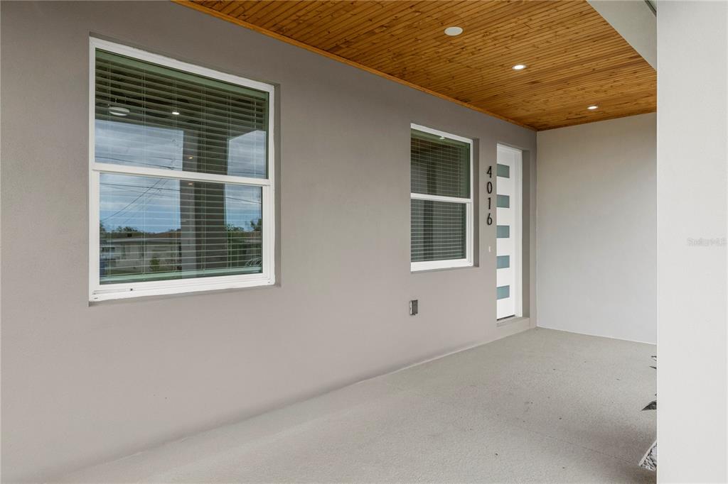 A covered porch features a gray wall, two windows, a modern front door, and wood-paneled ceiling — 4016 BADEN DRIVE, HOLIDAY, FL