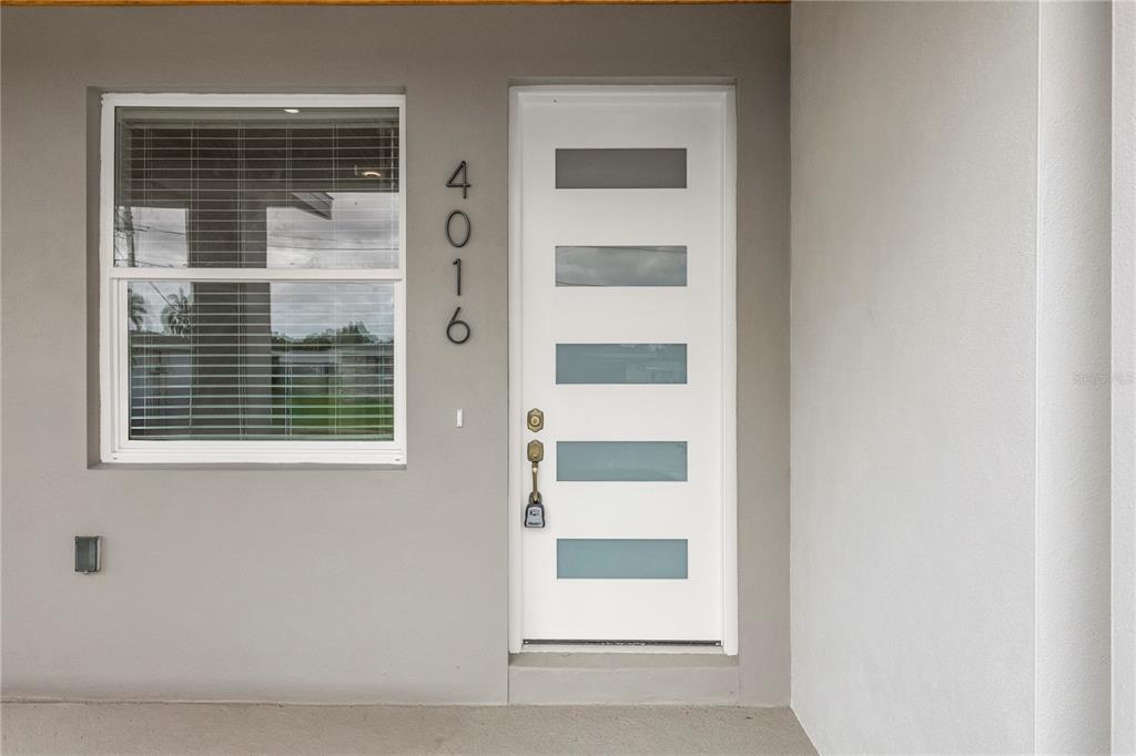 A white front door with five horizontal glass panels sits beside a window — 4016 BADEN DRIVE, HOLIDAY, FL