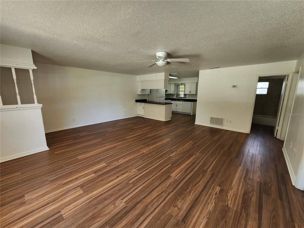 An open-concept living area with wood-look flooring leads to a kitchen with white cabinets — 2304 INDIA PALM DRIVE, EDGEWATER, FL