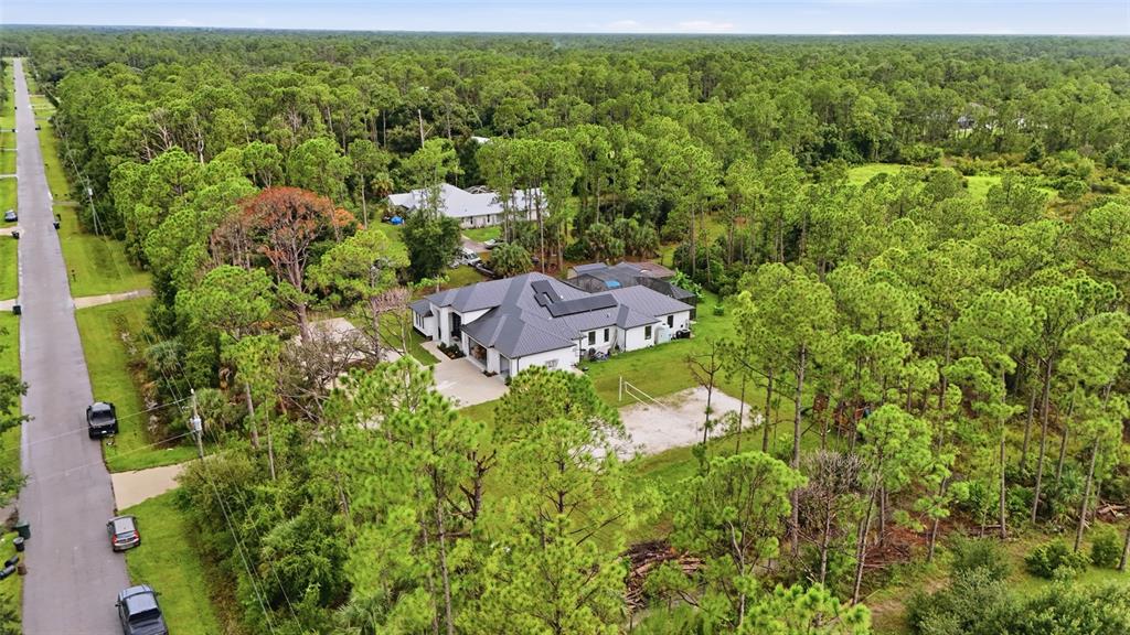 An aerial view shows a modern white house with a dark roof surrounded by pine trees — 6547 BEEDLA STREET, NORTH PORT, FL