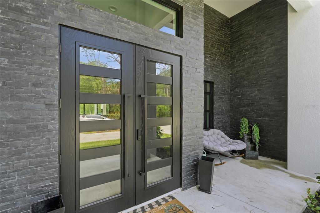 A modern entryway features a double glass door, dark stone veneer walls, and a rocking chair — 6547 BEEDLA STREET, NORTH PORT, FL
