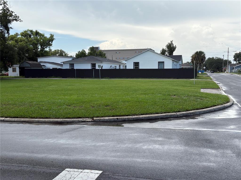 A large, grassy vacant lot sits behind a black fence in front of white houses — 1233 N NEW YORK AVENUE, LAKELAND, FL