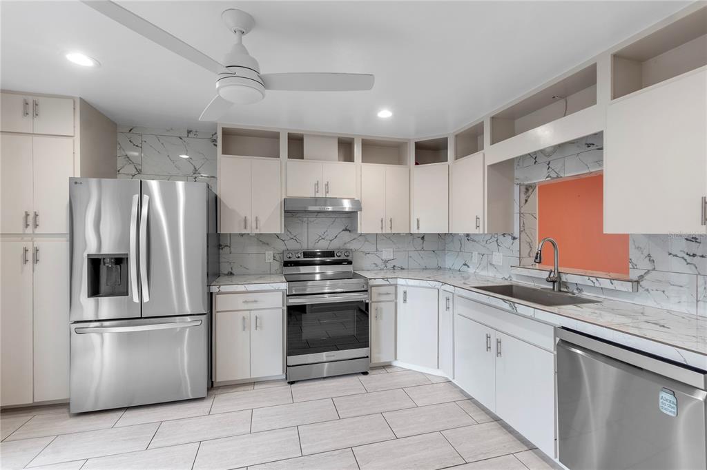 A kitchen features white cabinets, stainless steel appliances, marble-patterned countertops, and a white tile floor — 511 LAKESIDE DRIVE UNIT 511, BRADENTON, FL
